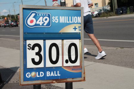 Photo for Lotto 649 5 million dollars thirty dollars gold ball logo sign outside outdoor exterior, with person jogging behind on sidewalk, blue white gold red - Royalty Free Image