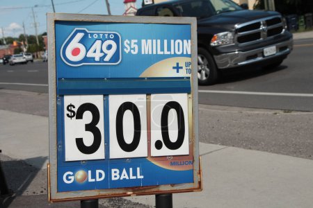 Photo for Lotto 649 5 million dollars thirty dollars gold ball logo sign outside outdoor exterior, truck driving toward sign behind on road, blue white gold red - Royalty Free Image