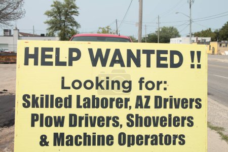 Photo for Help wanted looking for skilled laborer az drivers plow drivers shovelers and machine operators sign with road and sidewalk in background, yellow sign with black writing - Royalty Free Image