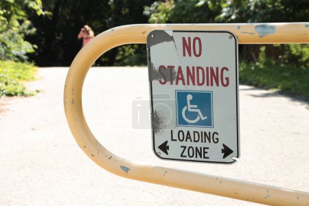 Foto de Ninguna zona de carga de pie con símbolo handicap y dos flechas que apuntan en dirección opuesta montadas en el carril de la puerta amarilla, persona en el fondo, blanco rojo azul y negro - Imagen libre de derechos