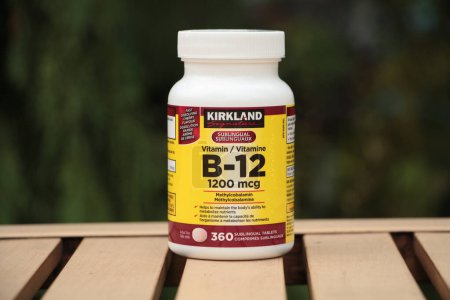 Photo for Kirkland vitamin b 12 1200mcg 360 tablets on outdoor light brown table with green behind, white yellow black burgundy - Royalty Free Image