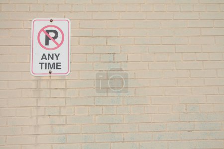 Photo for No parking any time symbol writing text rectangle horizontal sign on light beige brick wall, sign in top left corner, white black red - Royalty Free Image