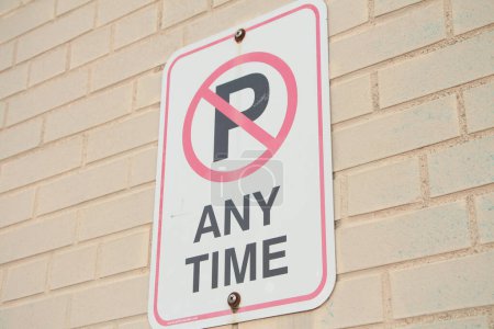 Photo for No parking any time symbol writing text rectangle horizontal sign on light beige brick wall, white black red, close up shot on angle - Royalty Free Image