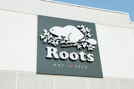 Foto de Raíces est 1973 signo logo en la parte delantera de la fachada de la tienda con ilustración de imagen de castor en ramas de hojas y el cielo azul detrás - Imagen libre de derechos