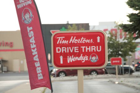Photo for Tim hortons wendys drive thru sign on post with breakfast wendys restaurant logo banner vertical red white flag next to it with cars behind - Royalty Free Image