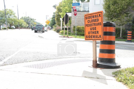 Photo for Sidewalk closed pedestrians use other sidewalk writing caption text orange black rectangle construction sign on sidewalk in front of traffic delineator pylon next to road street - Royalty Free Image