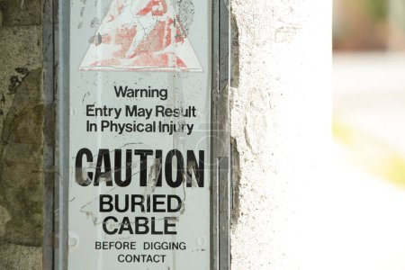 Photo for Warning entry may result in physical injury caution buried cable before digging contact the sign on cement concrete post with bright sun shining on one side and shade on the other - Royalty Free Image