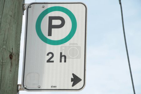 Photo for Parking allowed for 2 hours h white green black vertical rectangle sign left of frame with arrow and p in green circle on wood post with sky behind - Royalty Free Image