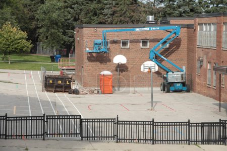 Photo for United rentals 4x4 four by four boom lift jack blue gray extended parked in elementary schoolyard with basketball nets - Royalty Free Image