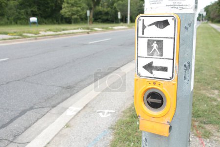 Photo for Crosswalk button large black silver circle yellow with illustration above of hand pressing button person walking and left arrow next to street road - Royalty Free Image