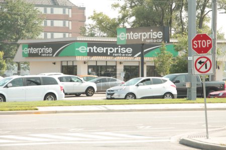 Foto de Empresa rent-a-car tienda tienda verde negro con el logotipo de la muestra disparado desde el otro lado de la calle con vehículos de tráfico de coches que pasan por delante - Imagen libre de derechos