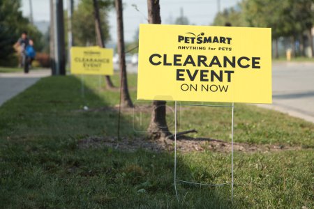 Photo for Petsmart anything for pets clearance event on now yellow sign on metal straight wires in grass next to road street with others behind and person - Royalty Free Image
