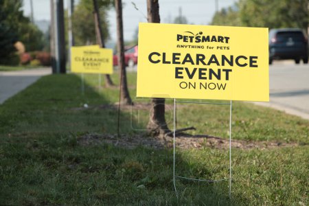 Photo for Petsmart anything for pets clearance event on now yellow sign on metal straight wires in grass next to road street with others behind and car turning in background into parking lot - Royalty Free Image