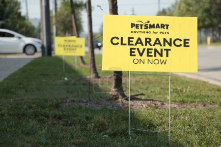 Photo for Petsmart anything for pets clearance event on now yellow sign on metal straight wires in grass next to road street with others behind and car vehicle exiting parking lot in background - Royalty Free Image