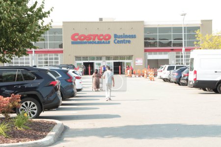 Photo for Costco wholesale business centre center with parking lot in front in summer with two customers people walking toward store with shopping cart buggy with its doors open - Royalty Free Image