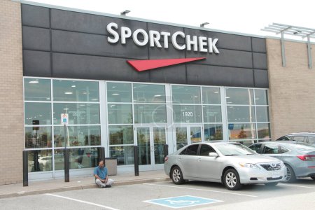 Photo for Sportchek apparel clothing sports athlete athletic store front entrance exterior with cars vehicles and logo sign on front and person sitting on curb sidewalk, shot on angle - Royalty Free Image