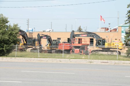 Photo for Parked construction machinery equipment next to road street behind fence next to building in summer - Royalty Free Image