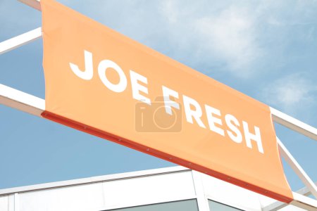 Téléchargez les photos : Joe marque fraîche logo publicité bannière drapeau signe horizontal rectangle sur barres métalliques fond orange blanc écriture extérieure avec ciel nuages bâtiment derrière - en image libre de droit