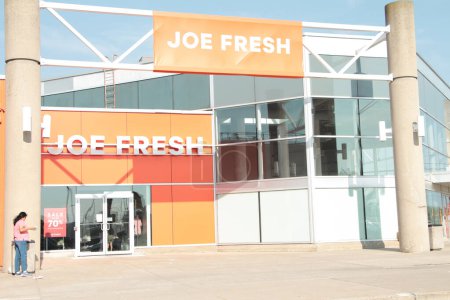 Photo for Joe fresh brand company store building front entrance with banner flag sign horizontal rectangle on metal bars orange background white writing exterior outside with person in front - Royalty Free Image