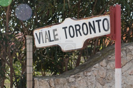 Foto de Viale toronto street road sign with trees and stone fence behind pachino sicily italy writing caption text white black red, close up - Imagen libre de derechos