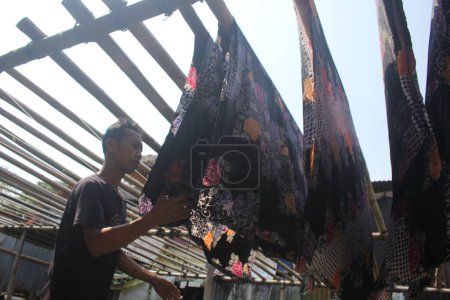 Téléchargez les photos : Pekalongan, Indonésie - juillet 05, 2023 : Homme séchant du tissu batik sur la cour. - en image libre de droit