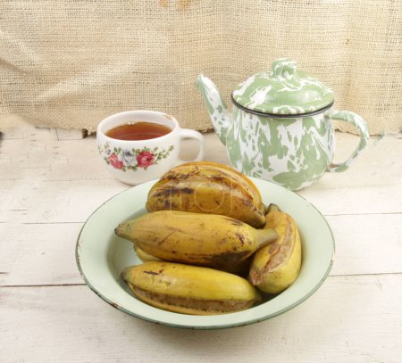 Foto de Un plato de plátano de vapor con una taza de té caliente en la mesa - Imagen libre de derechos