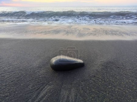 Photo for Black stone on black sand of volcanic beach of Saint Paul, Reunion. Zen background with isolated round black stone - Royalty Free Image