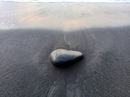 Photo for Black stone on black sand, volcanic beach of Saint Paul, Reunion. Zen background with isolated round black stone - Royalty Free Image
