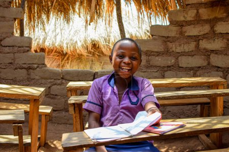 Foto de Retrato de un niño africano aprendiendo en una comunidad rural.Niños africanos sonrientes con uniforme escolar en un aula. Educación primaria en aldeas africanas. - Imagen libre de derechos