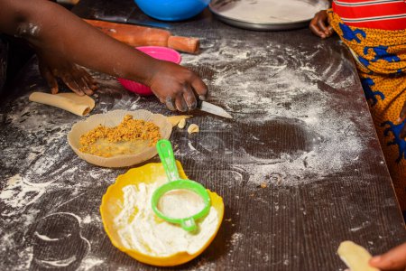 Téléchargez les photos : Fabrication de pâtisseries avec des ingrédients africains locaux. Fabriquer de la farine à la main d'un boulanger. Table de pétrissage dans une classe pratique alimentaire. Préparation des tartes pour la cuisson au four. - en image libre de droit