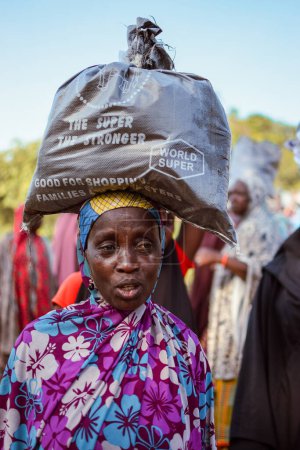 Téléchargez les photos : Abuja, Nigeria - 26 février 2023 : Femme avec un sac sur la tête. Community Sensitization on Covid 19, Health and Water Hygiene. Africains assis, faisant la queue et attendant des soins médicaux gratuits - en image libre de droit