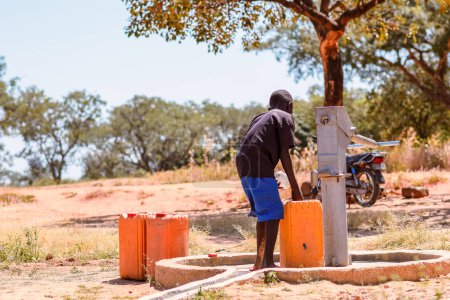 Foto de Talata, Plateau State - 2 de abril de 2023: Indígena africana que extrae agua de una bomba de mano india recién construida. Miembros de la comunidad que buscan agua para uso doméstico. - Imagen libre de derechos