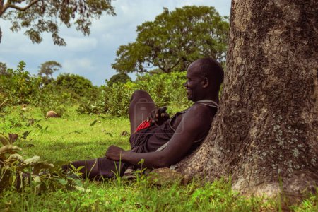 Photo for Plateau, Nigeria - April 5, 2023: African Man Taking a Rest in Nature After a Long Day Farming. Beautiful Scenery of the African Woods. - Royalty Free Image