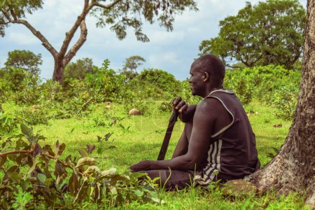 Foto de Plateau, Nigeria - 5 de abril de 2023: El hombre africano descansa en la naturaleza después de un largo día de agricultura. Hermoso paisaje de los bosques africanos. - Imagen libre de derechos