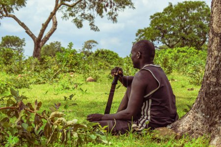 Foto de Plateau, Nigeria - 5 de abril de 2023: El hombre africano descansa en la naturaleza después de un largo día de agricultura. Hermoso paisaje de los bosques africanos. - Imagen libre de derechos