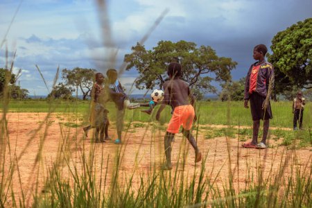 Foto de Lagos, Nigeria - 02 de marzo de 2023: Niños africanos jugando al fútbol en un campo de arena. Actividades deportivas en comunidades rurales de África. Fútbol callejero entre niños africanos locales. - Imagen libre de derechos