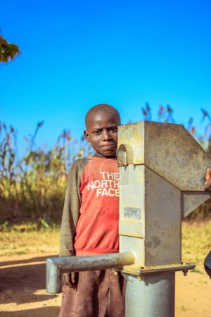 Téléchargez les photos : Abuja, Nigéria - 02 mars 2023 : Un enfant africain récupère de l'eau propre sous le soleil dans une communauté rurale. Des gens joyeux et reconnaissants. - en image libre de droit