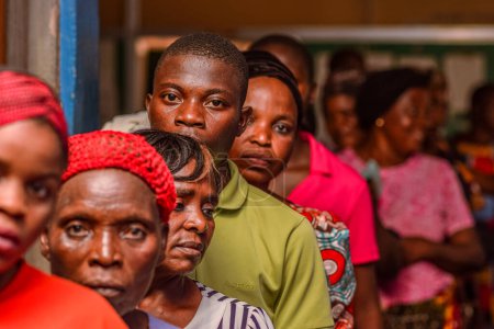 Foto de Abuja, Nigeria - 10 de febrero de 2021: Africanos sentados, haciendo cola y esperando atención médica gratuita en una comunidad rural. La gente se registra para votar en las elecciones. Ejercicio de campaña política - Imagen libre de derechos