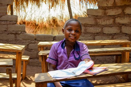 Foto de Abuja, Nigeria - 6 de mayo de 2023: Retrato de un niño africano aprendiendo en una comunidad rural. Sonriente niño africano con uniforme escolar en un aula. Educación primaria en aldeas africanas. - Imagen libre de derechos