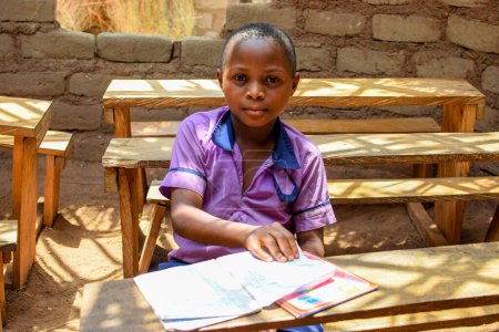Téléchargez les photos : Abuja, Nigéria - 6 mai 2023 : Portrait d'un enfant africain apprenant dans une communauté rurale. Un enfant africain souriant portant un uniforme scolaire dans une salle de classe. Enseignement primaire dans les villages africains. - en image libre de droit