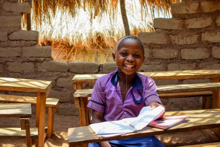Foto de Abuja, Nigeria - 6 de mayo de 2023: Retrato de un niño africano aprendiendo en una comunidad rural. Sonriente niño africano con uniforme escolar en un aula. Educación primaria en aldeas africanas. - Imagen libre de derechos