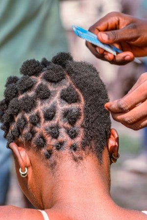 Téléchargez les photos : Abuja Nigeria - 20 juin 2023 : Femme Africaine Plaquant ses Cheveux. Stylish Cultural Hair Designs among African Women. Salon de coiffure dans la communauté rurale nigériane - en image libre de droit