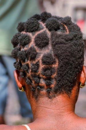 Foto de Abuja Nigeria - 20 de junio de 2023: African Woman Plating her Hair. Elegantes diseños de cabello cultural entre las mujeres africanas. Peluquería en comunidad rural nigeriana - Imagen libre de derechos