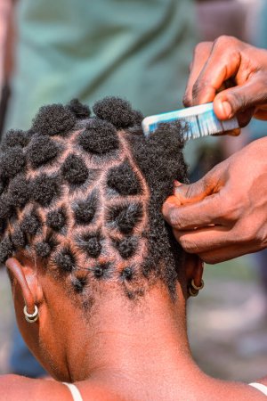 Photo for Abuja Nigeria - June 20, 2023: African Woman Plating her Hair. Stylish Cultural Hair Designs among African Women. Hair Dressing Salon in Nigerian Rural Community - Royalty Free Image