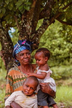 Photo for Abuja, Nigeria - June 5, 2023: Elderly African Senior spending playing with her children. Grandmother and her grandchildren. Mother outdoor sitting under a tree - Royalty Free Image