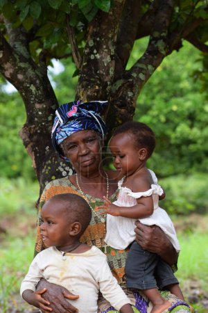Téléchargez les photos : Abuja, Nigéria - 5 juin 2023 : Aînée Africaine Aînée passe son temps à jouer avec ses enfants. Grand-mère et ses petits-enfants. Mère assise en plein air sous un arbre - en image libre de droit