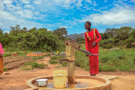 Téléchargez les photos : Karara, État de Nasarawa, Nigéria - 5 mai 2021 : Une femme africaine utilise un puits de pompage à main indien nouvellement construit dans une communauté rurale d'Afrique. Eau courante provenant d'un point d'eau de forage communautaire - en image libre de droit
