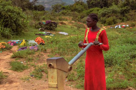 Foto de Karara, estado de Nasarawa, Nigeria - 5 de mayo de 2021: Mujer Africana usando la bomba de mano india recién construida Borewell en una comunidad rural de África. Agua corriente desde un punto de agua de pozo comunitario - Imagen libre de derechos