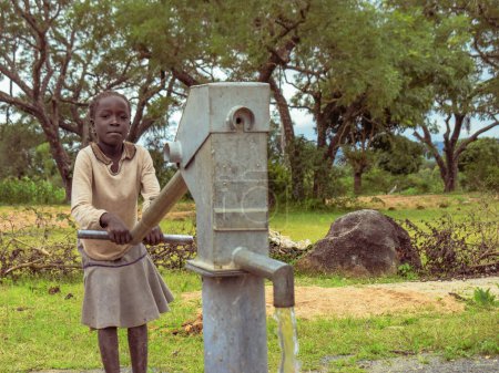 Téléchargez les photos : Karara, État de Nasarawa, Nigéria - 5 mai 2021 : Fille utilisant un puits de forage à pompe à main indien dans une communauté rurale en Afrique. Eau courante provenant d'un point d'eau de forage communautaire - en image libre de droit
