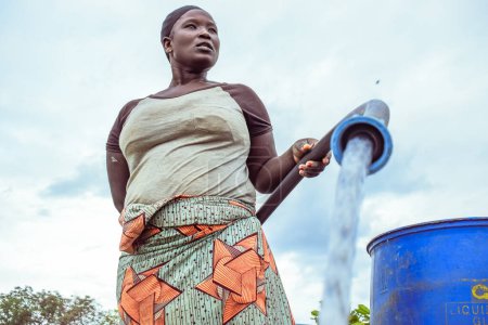 Téléchargez les photos : Abuja, Nigéria - 8 octobre 2022 : Femme africaine qui va chercher de l'eau. Clean Water Solution in African Community ". Happy African Récupération d'eau dans un seau - en image libre de droit